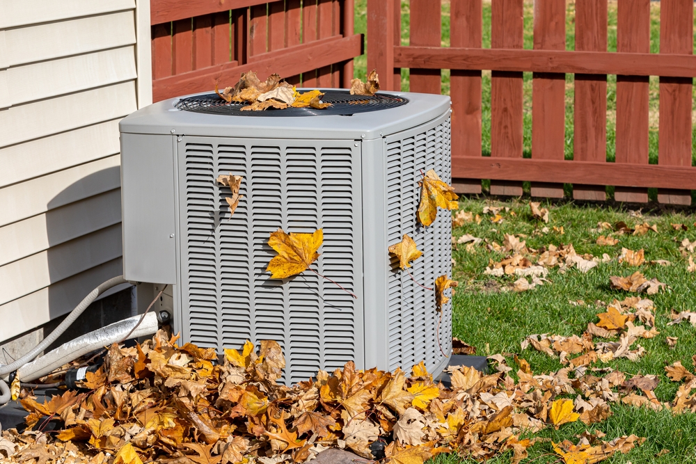 Dirty outdoor HVAC unit covered in fall leaves that needs to be cleaned